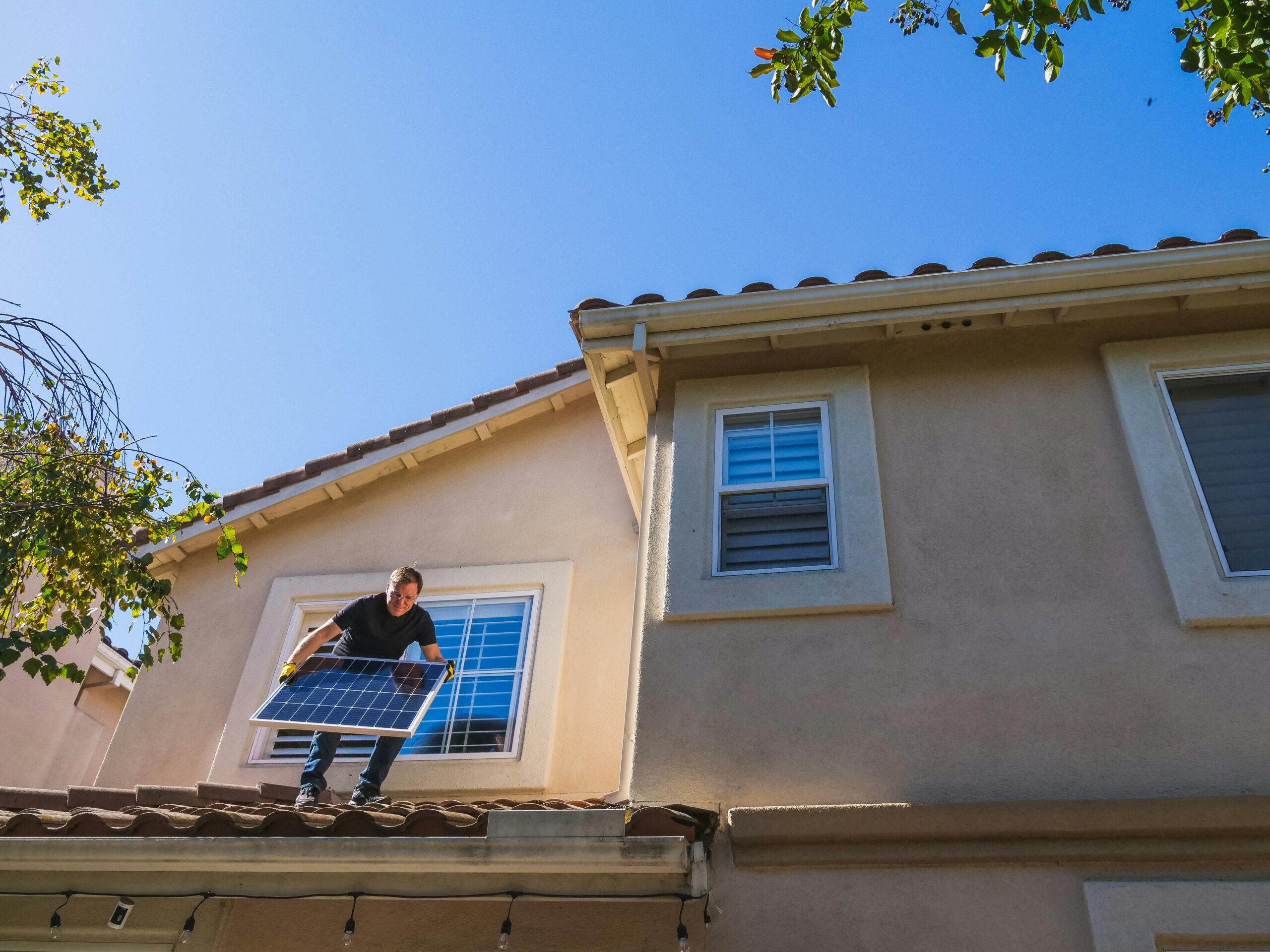 Man installing a solar panel on a rooftop under a clear blue sky, promoting renewable energy.